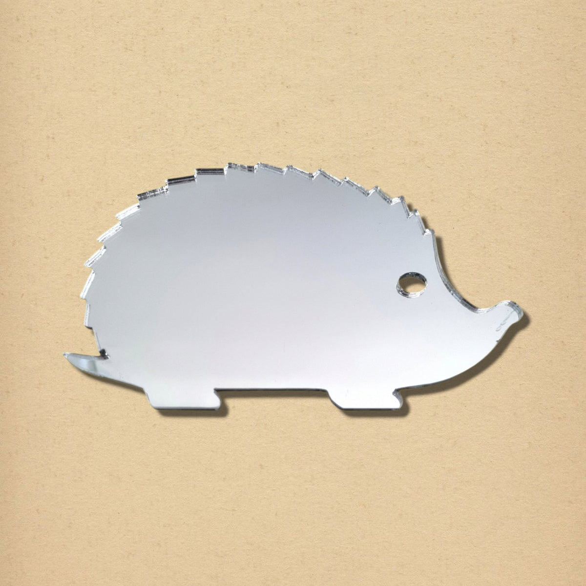 A silver hedgehog-shaped mirror with spiky back details on a textured beige background.