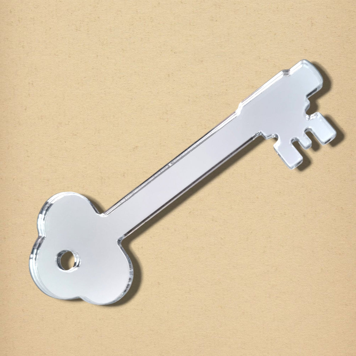 A silver key-shaped mirror resting flat on a textured tan background.