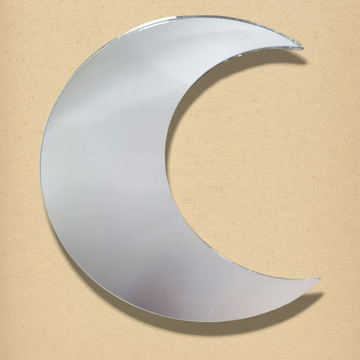 Crescent moon-shaped mirror in reflective silver, displayed against a neutral tan background.