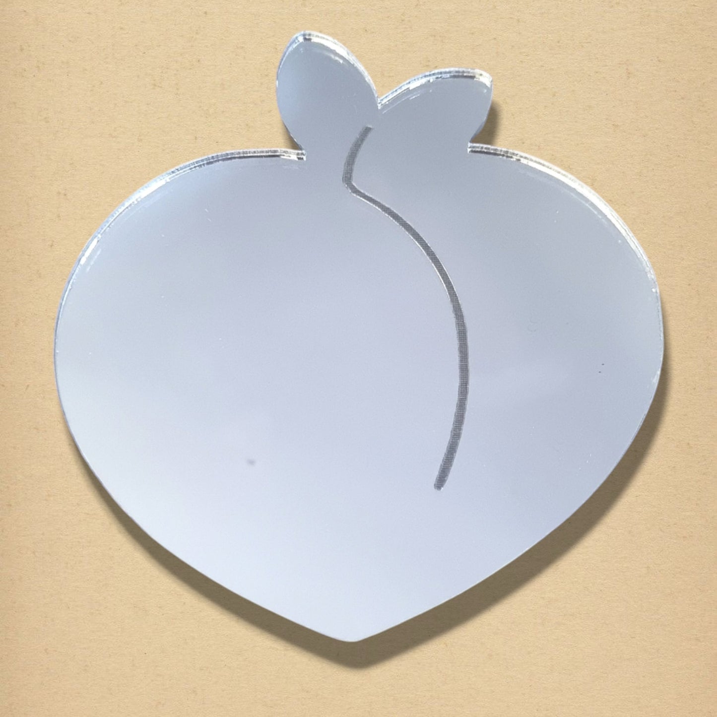 Peach-shaped acrylic mirror with two small leaves at the top and an engraved vertical line.