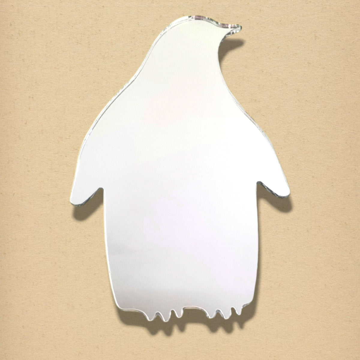A silver penguin-shaped mirror on a textured beige background.