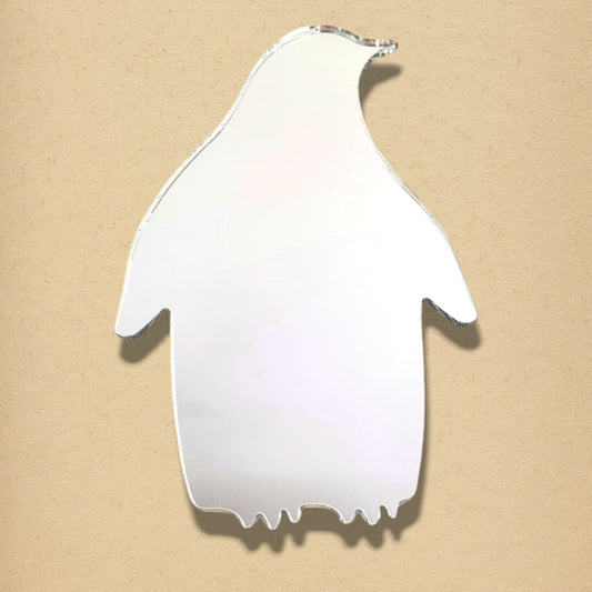 A silver penguin-shaped mirror on a textured beige background.