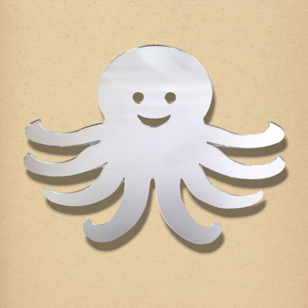 Silver octopus-shaped mirror with a smiling face cut-out, against a tan background.