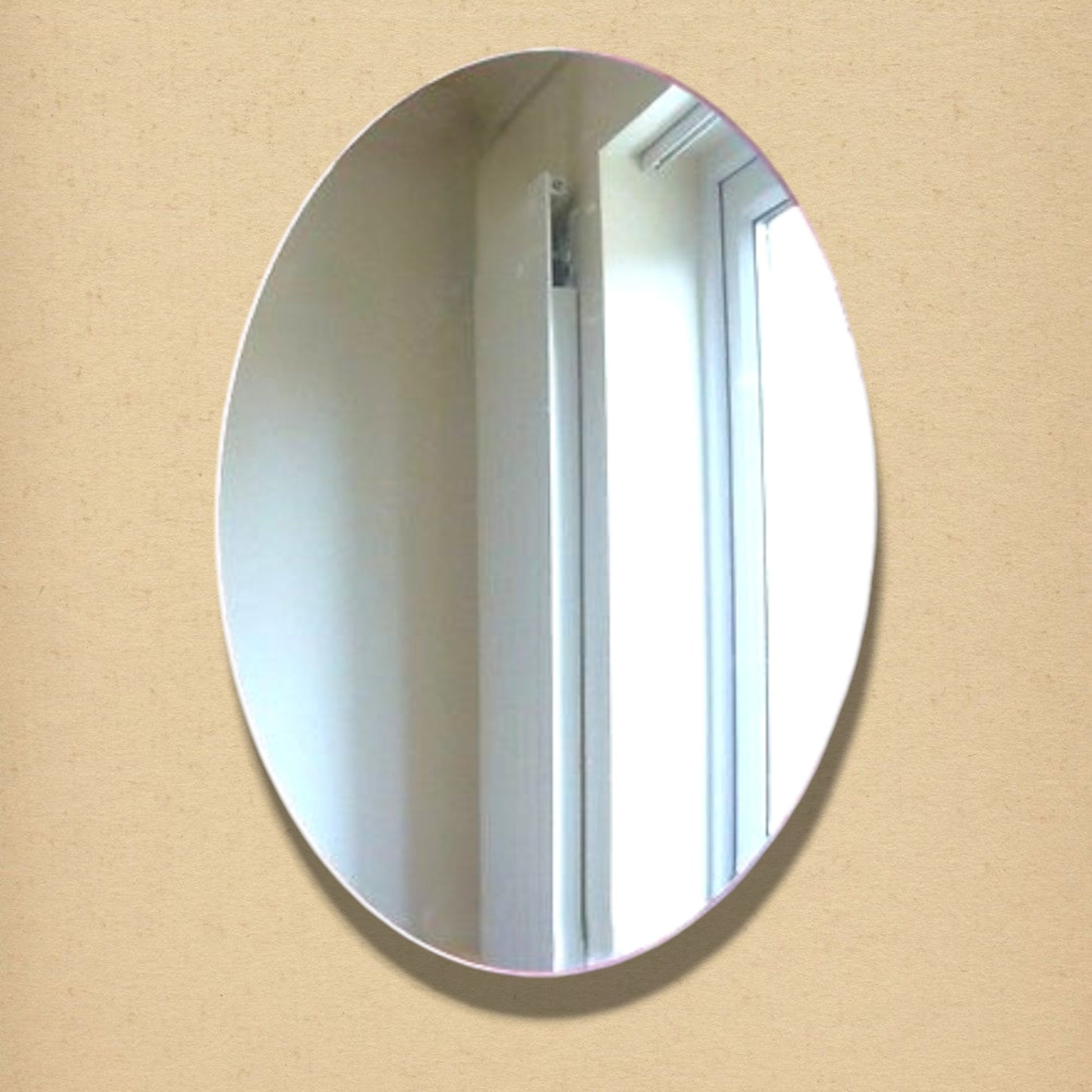 Simple frameless vertical oval mirror mounted on a beige wall, reflecting a bright indoor room.