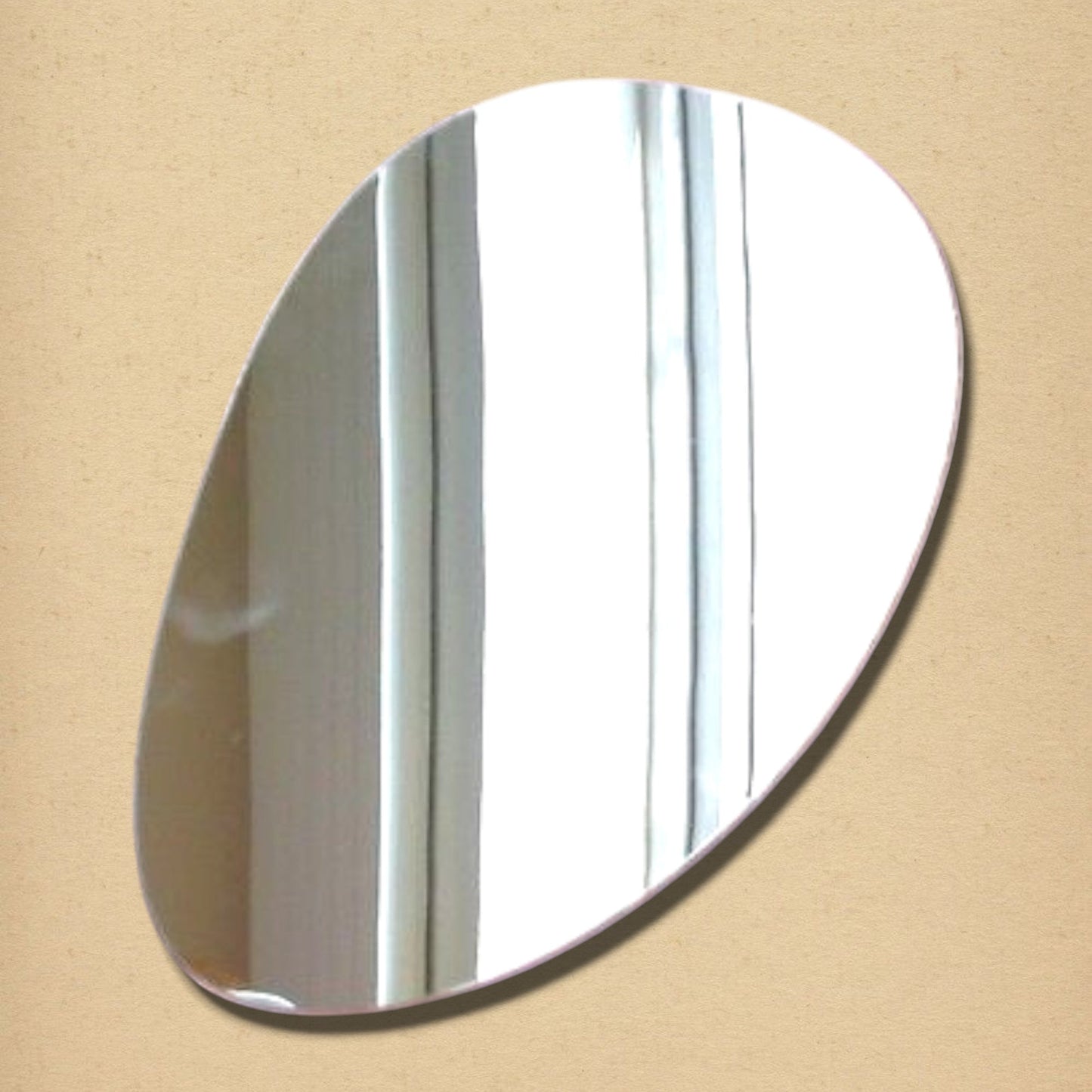 An asymmetrical pebble-shaped wall mirror with reflective glass on a neutral background.