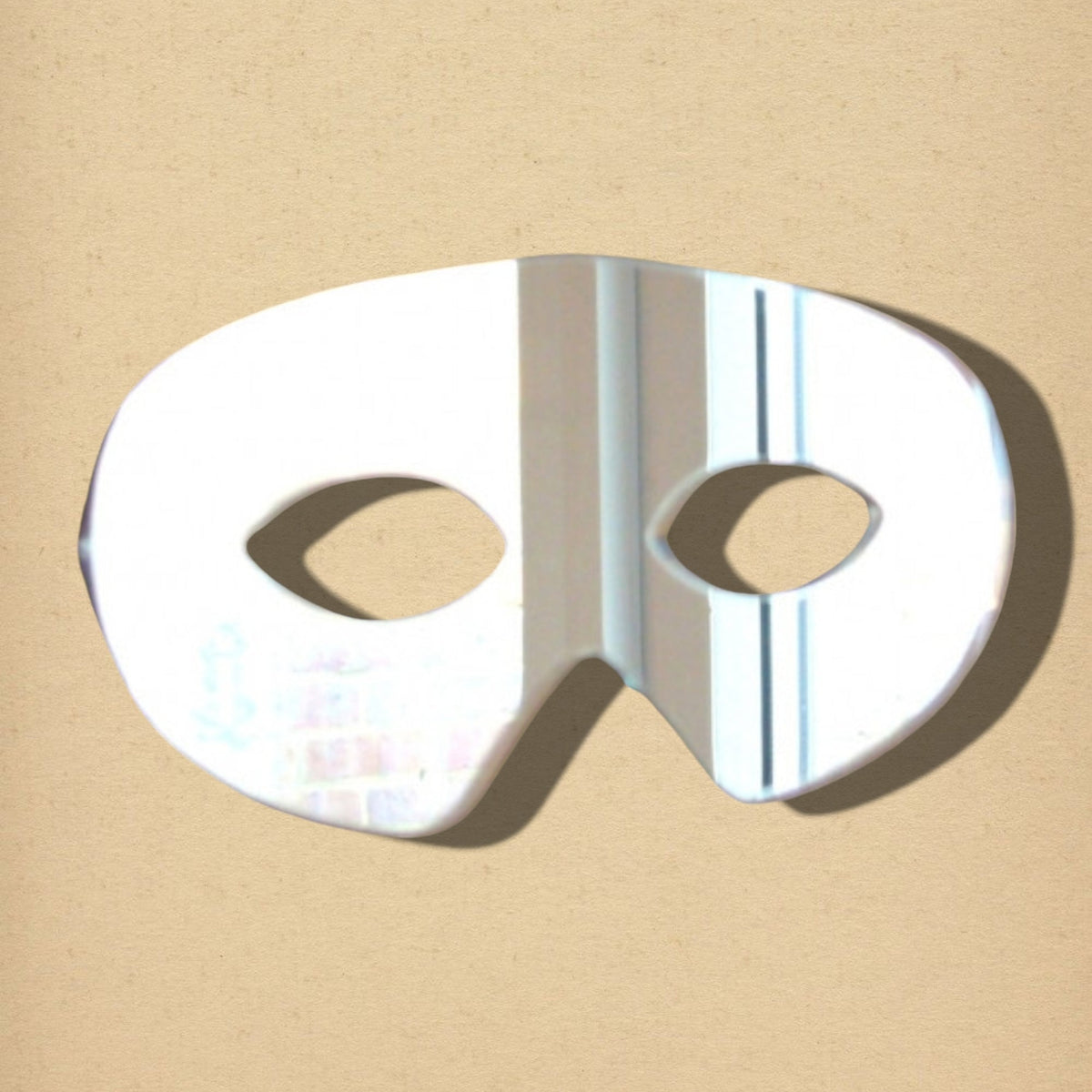 Zorro-style masquerade mask mirror with a reflective surface and two eye holes on a beige background.