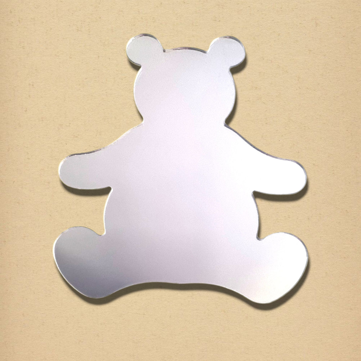 Teddy bear-shaped silver mirror on a light tan textured background.