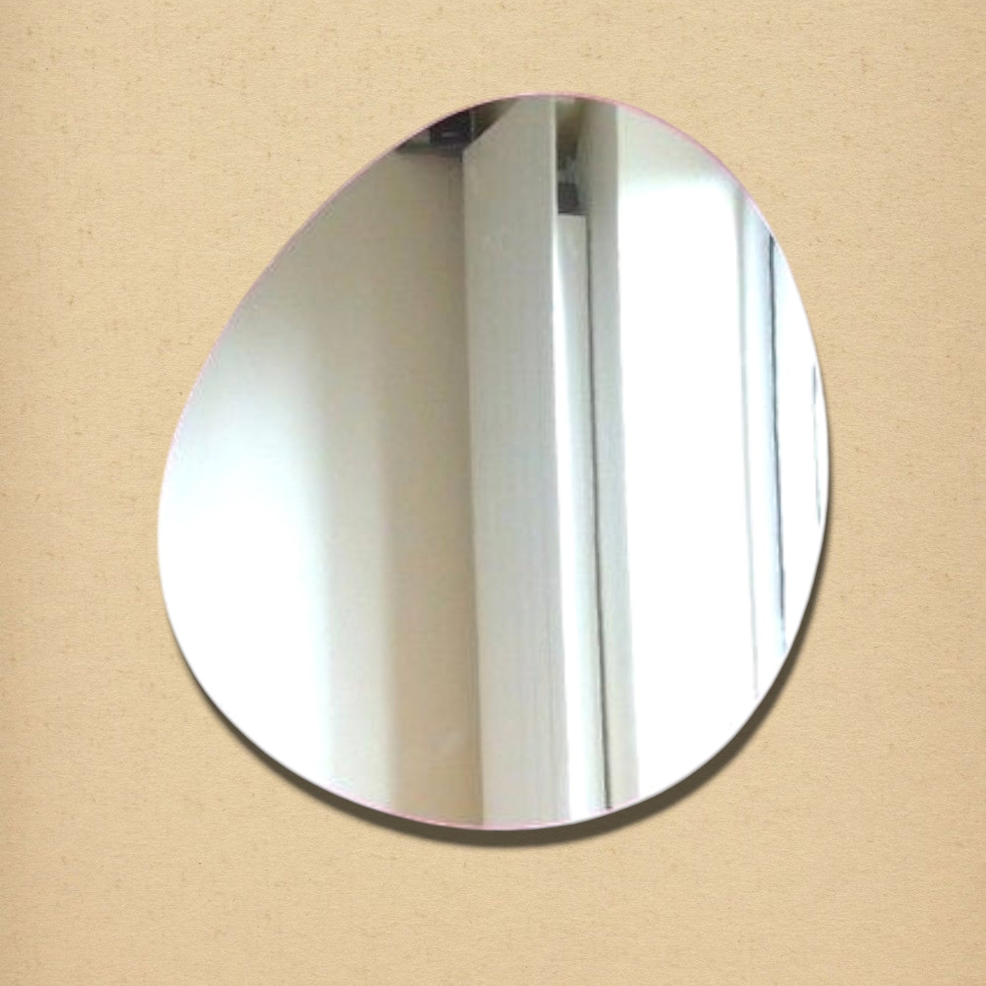 Asymmetric pebble-shaped wall mirror with a rounded, organic silhouette, mounted against a plain neutral background.
