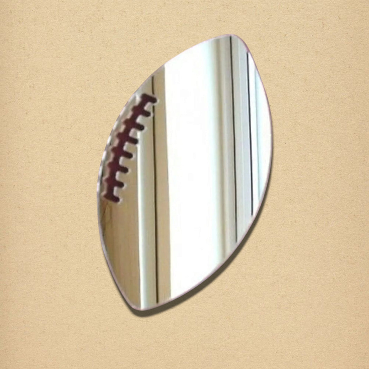 Rugby ball-shaped mirror with dark brown laces on a neutral background.