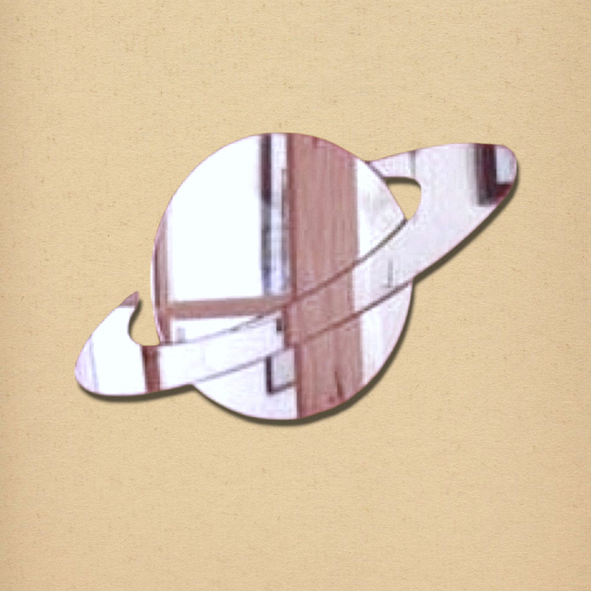Saturn-shaped mirror with a reflective surface and angled rings, on a textured beige background.
