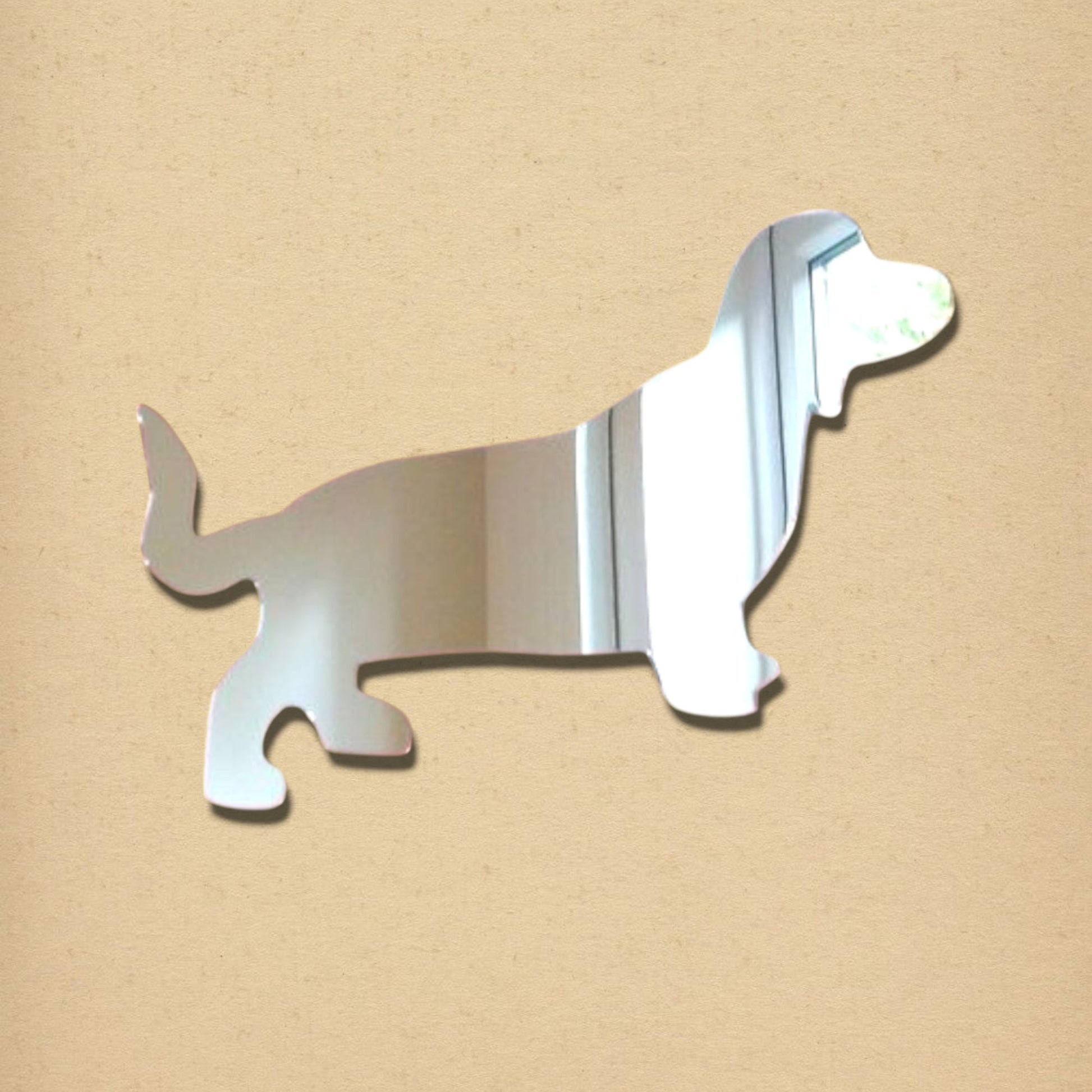 Dachshund-shaped reflective silver acrylic mirror on a light textured background.