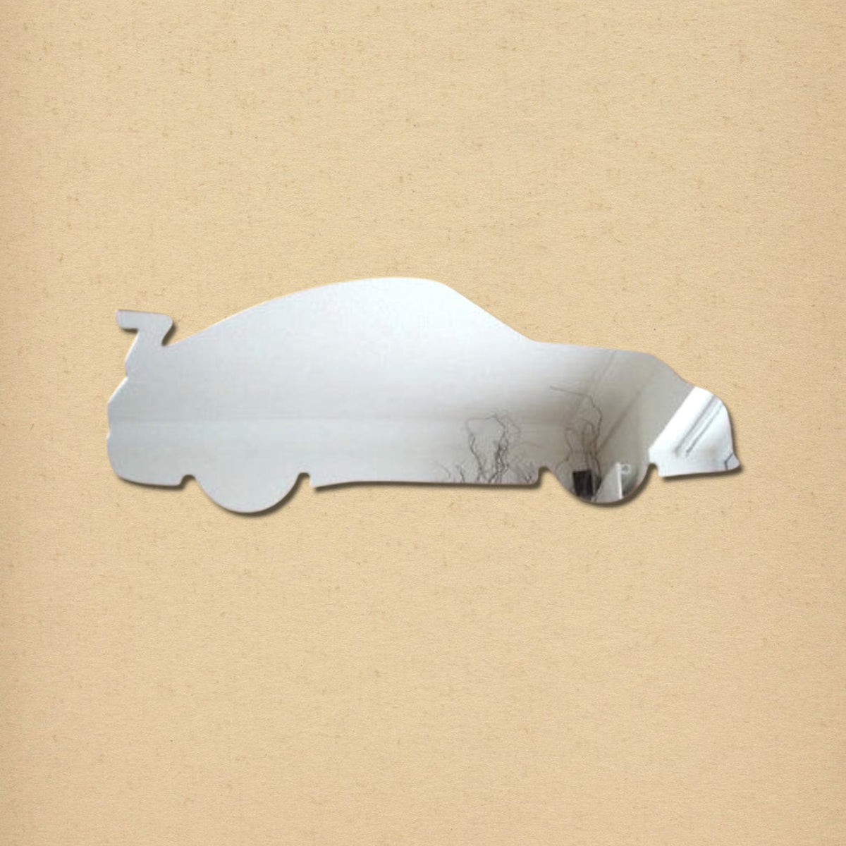 A reflective sports car-shaped wall mirror with a spoiler against a tan background.