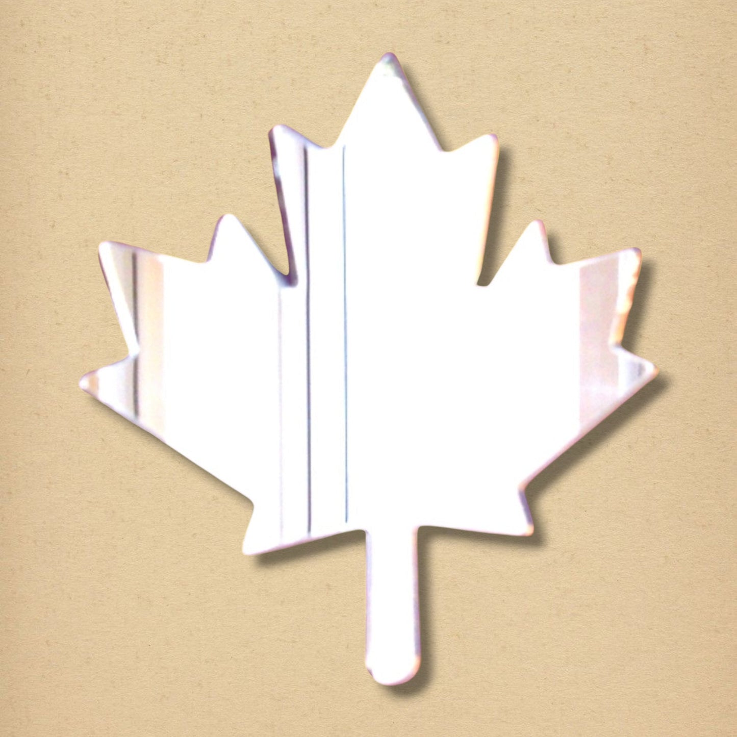 Maple leaf-shaped acrylic mirror on a textured tan background.