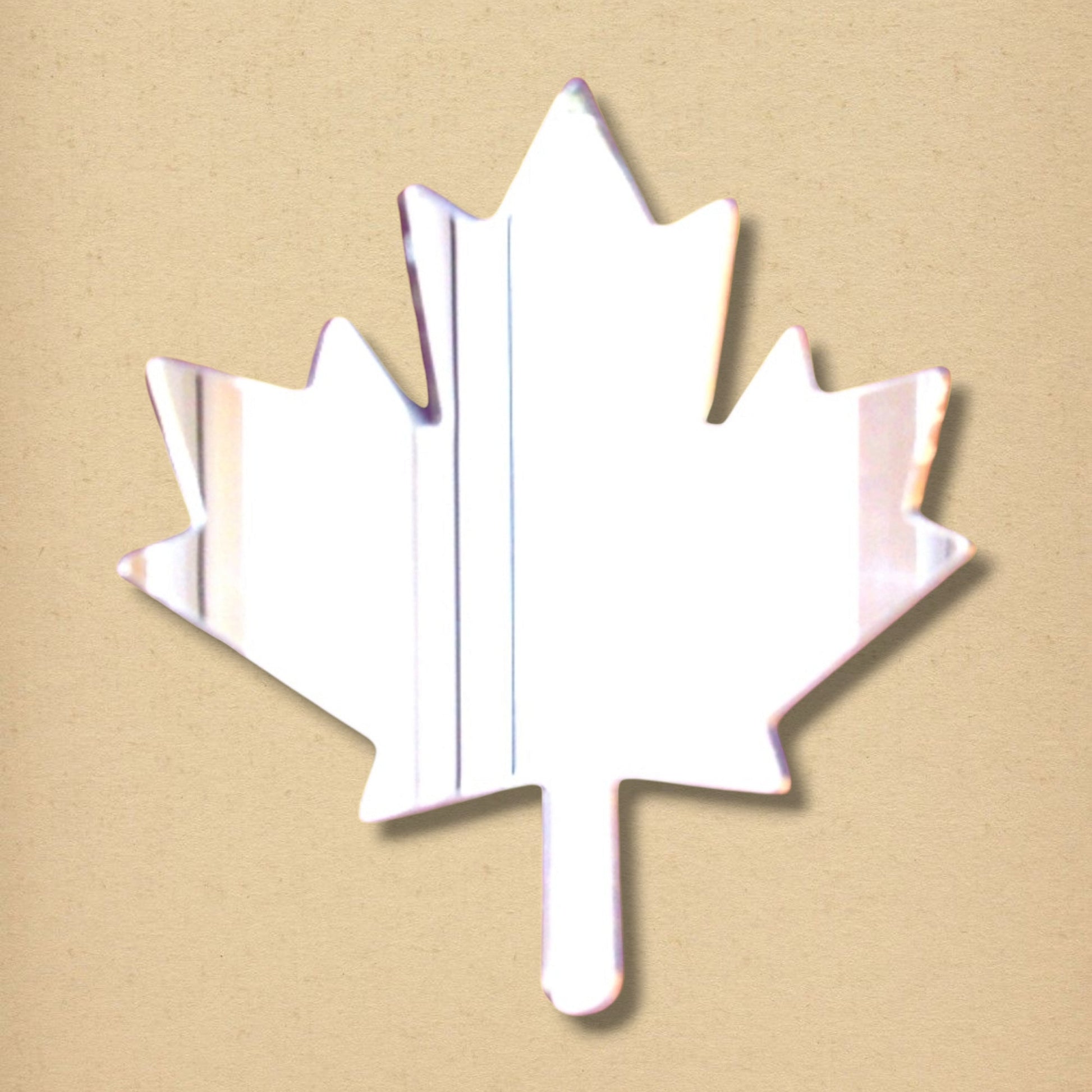 Maple leaf-shaped acrylic mirror on a textured tan background.