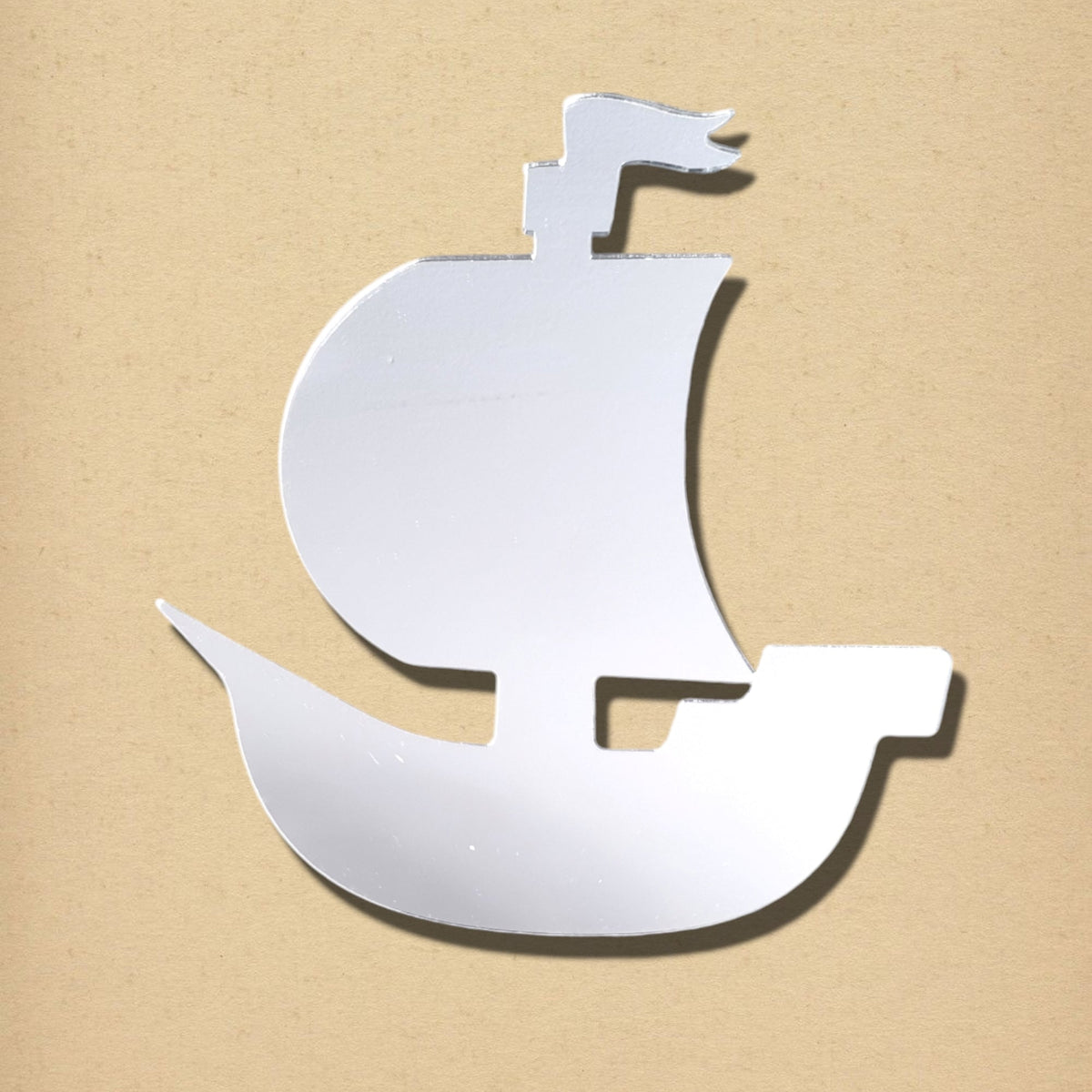 Silver pirate ship shaped mirror on a tan background.