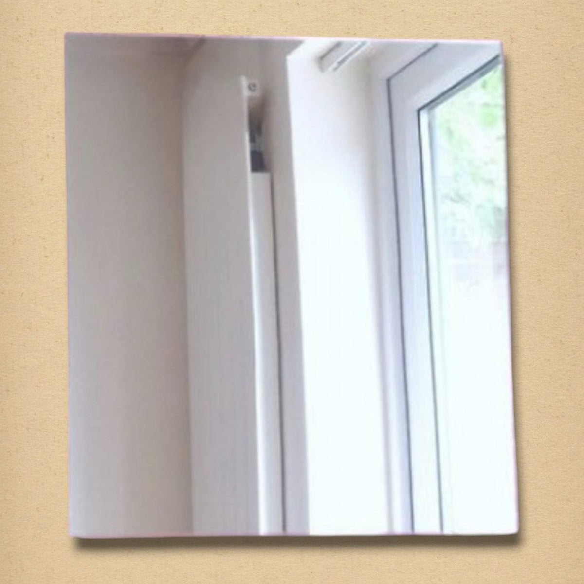 A frameless square mirror reflecting a white wall and window.
