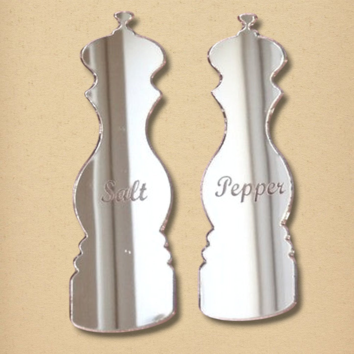 Two salt and pepper mill shaped mirrors engraved with Salt and Pepper on a beige background.
