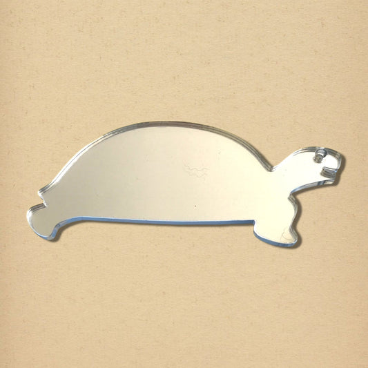 Tortoise-shaped reflective mirror on a light tan background.