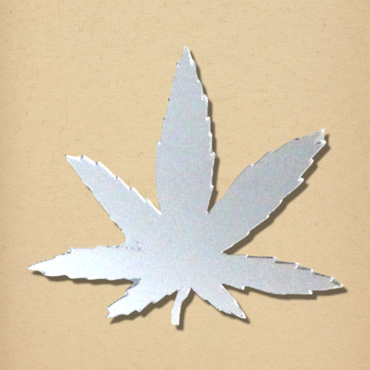 A silver, marijuana leaf-shaped wall mirror with jagged edges on a neutral tan background.