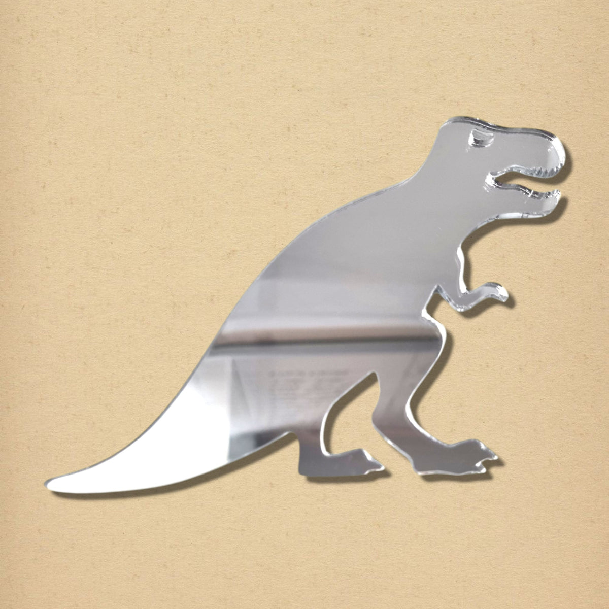Silver acrylic T-Rex dinosaur-shaped mirror against a tan background.