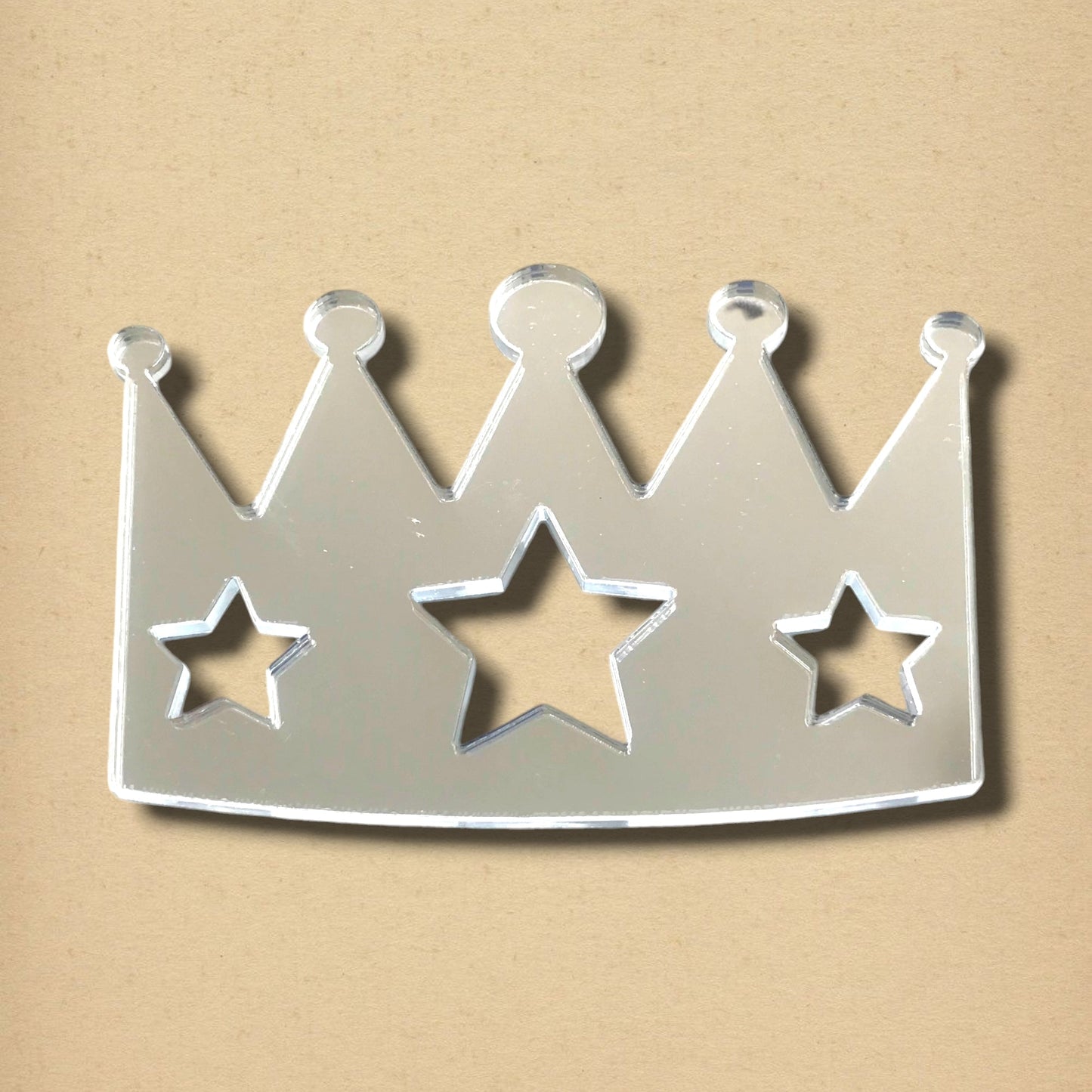 Crown-shaped mirror with three star cutouts, featuring a reflective surface against a beige background.