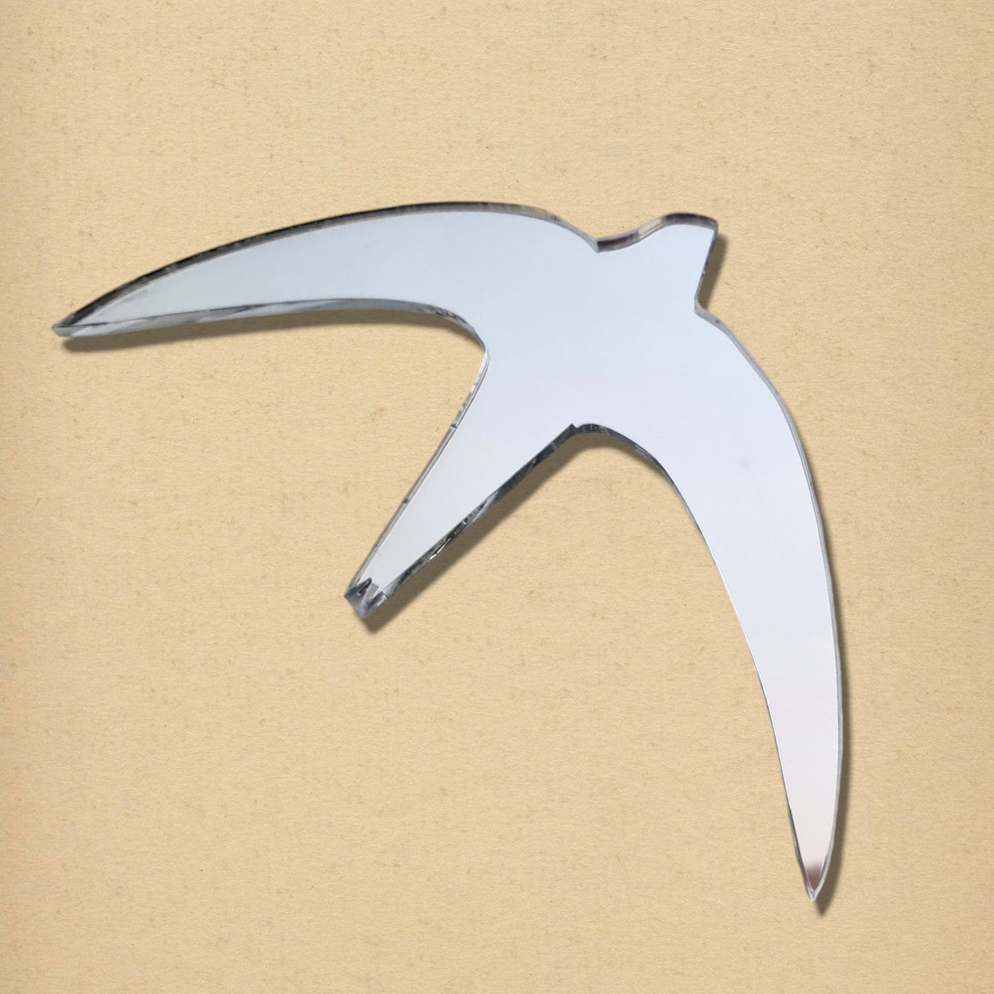 A silver acrylic mirror in the shape of a swift bird in flight against a tan background.