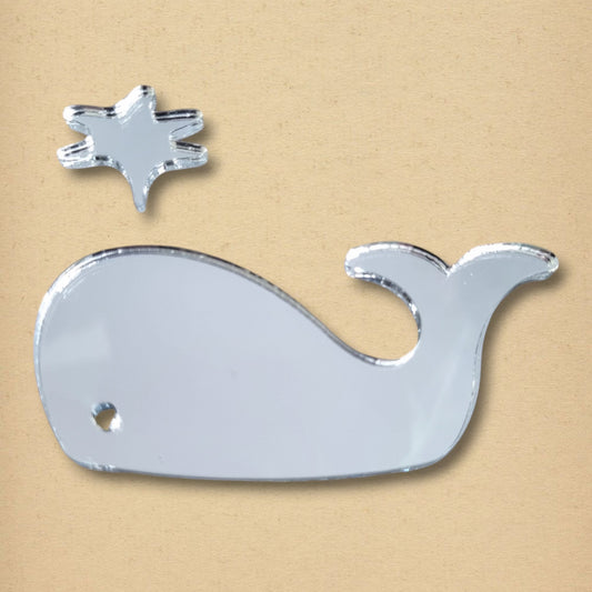 A silver whale-shaped mirror and a small starfish mirror are arranged on a tan surface.
