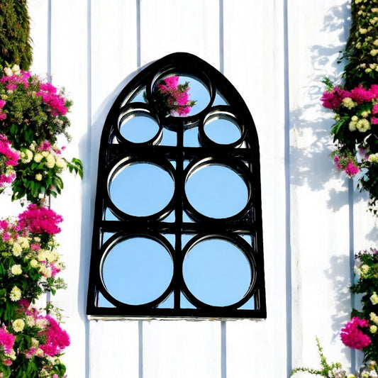 Gothic arch black-framed garden mirror with multiple circular panes, mounted on a white wall.