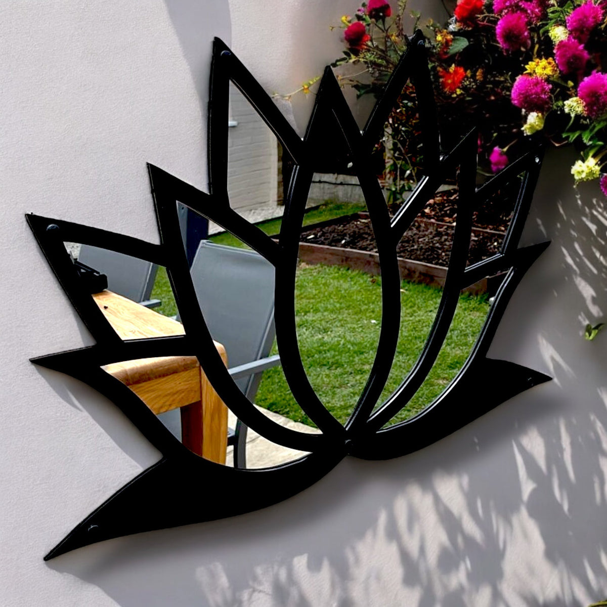 Black lotus flower-shaped metal framed garden mirror mounted on a white wall.
