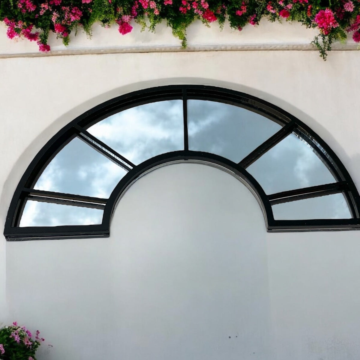 Black half-arch window garden mirror with gridded glass panels mounted on a plain white wall.