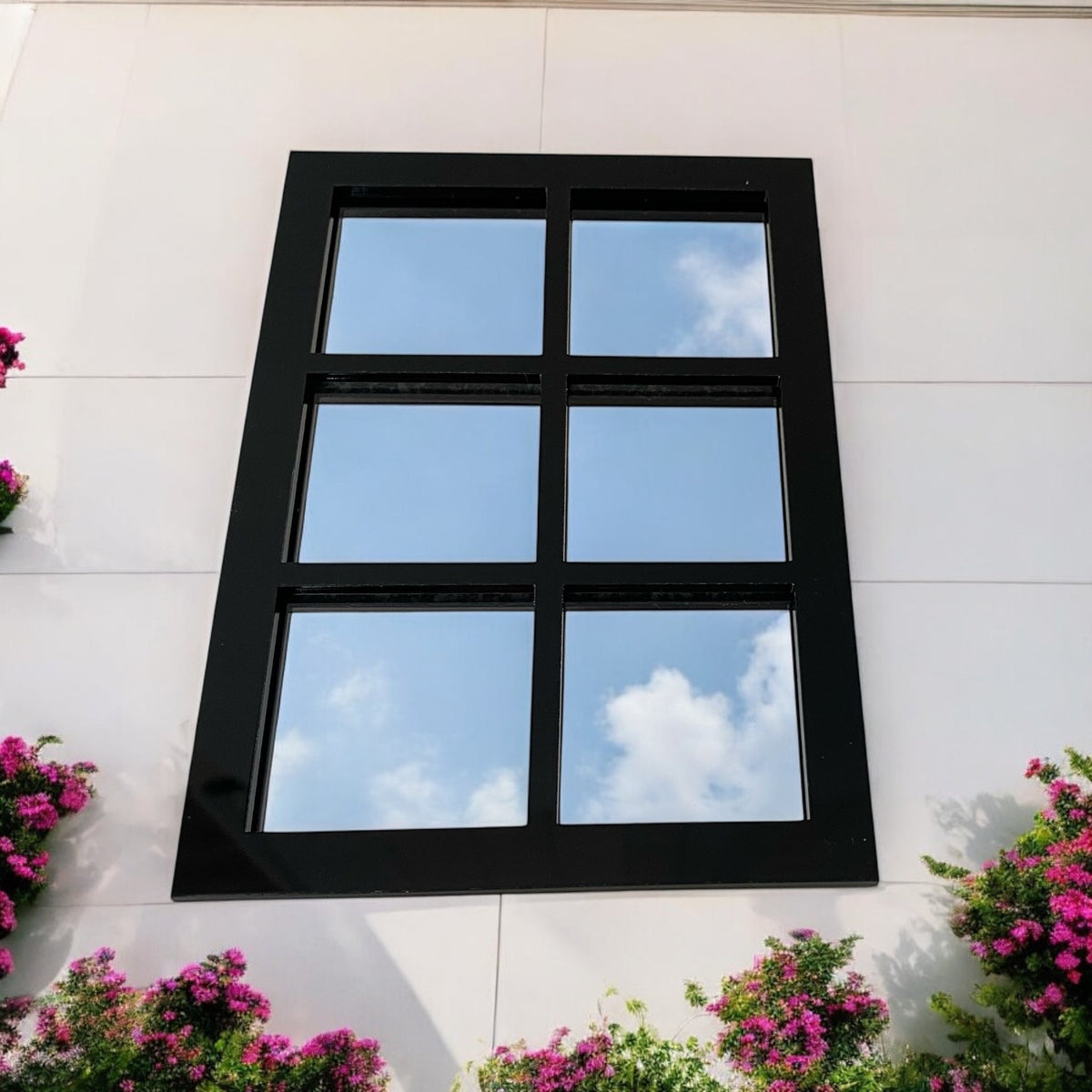 Rectangular black-framed six-panel garden mirror mounted on a white wall, reflecting a blue sky.