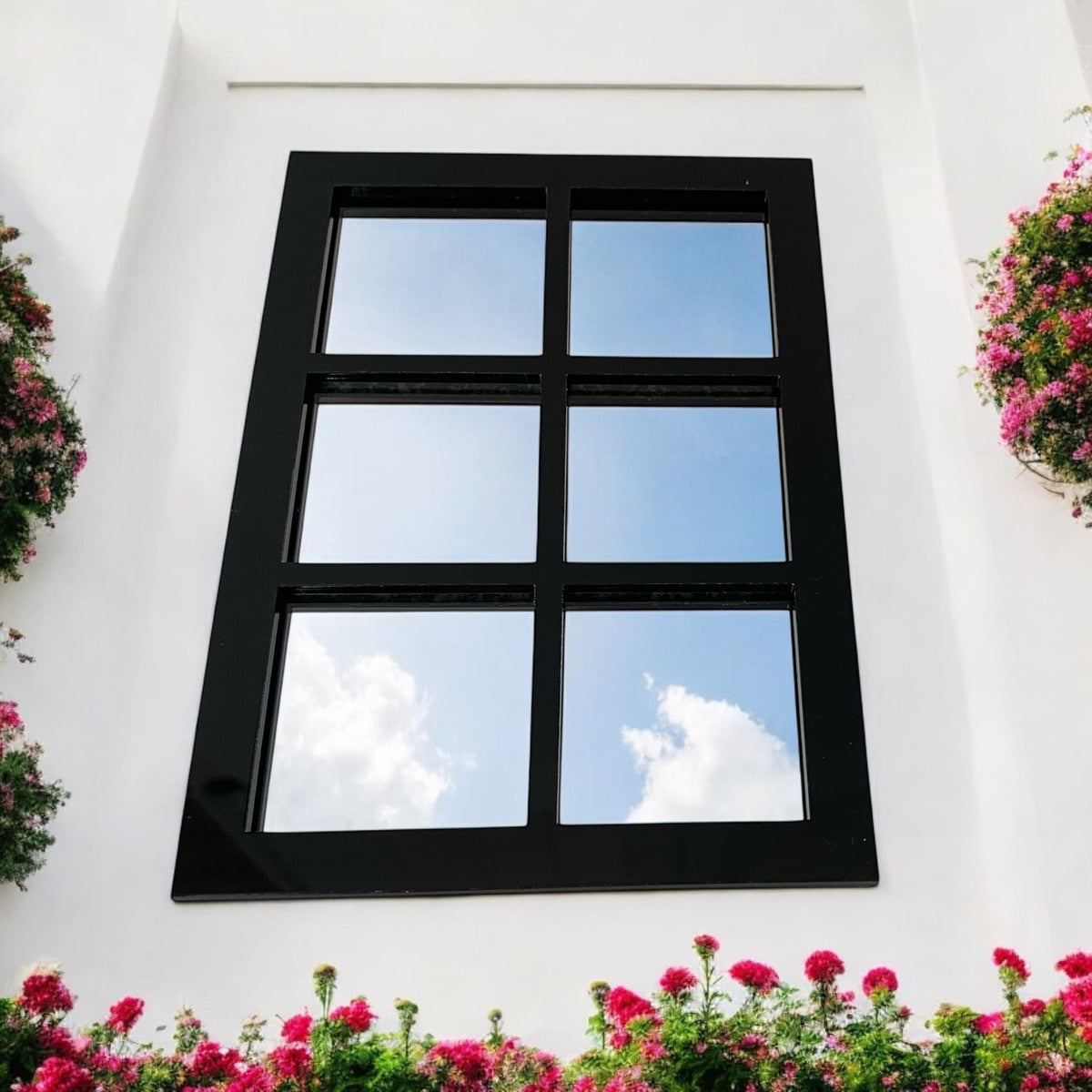 A rectangular black six-panel garden mirror mounted on a white wall with pink flowers.