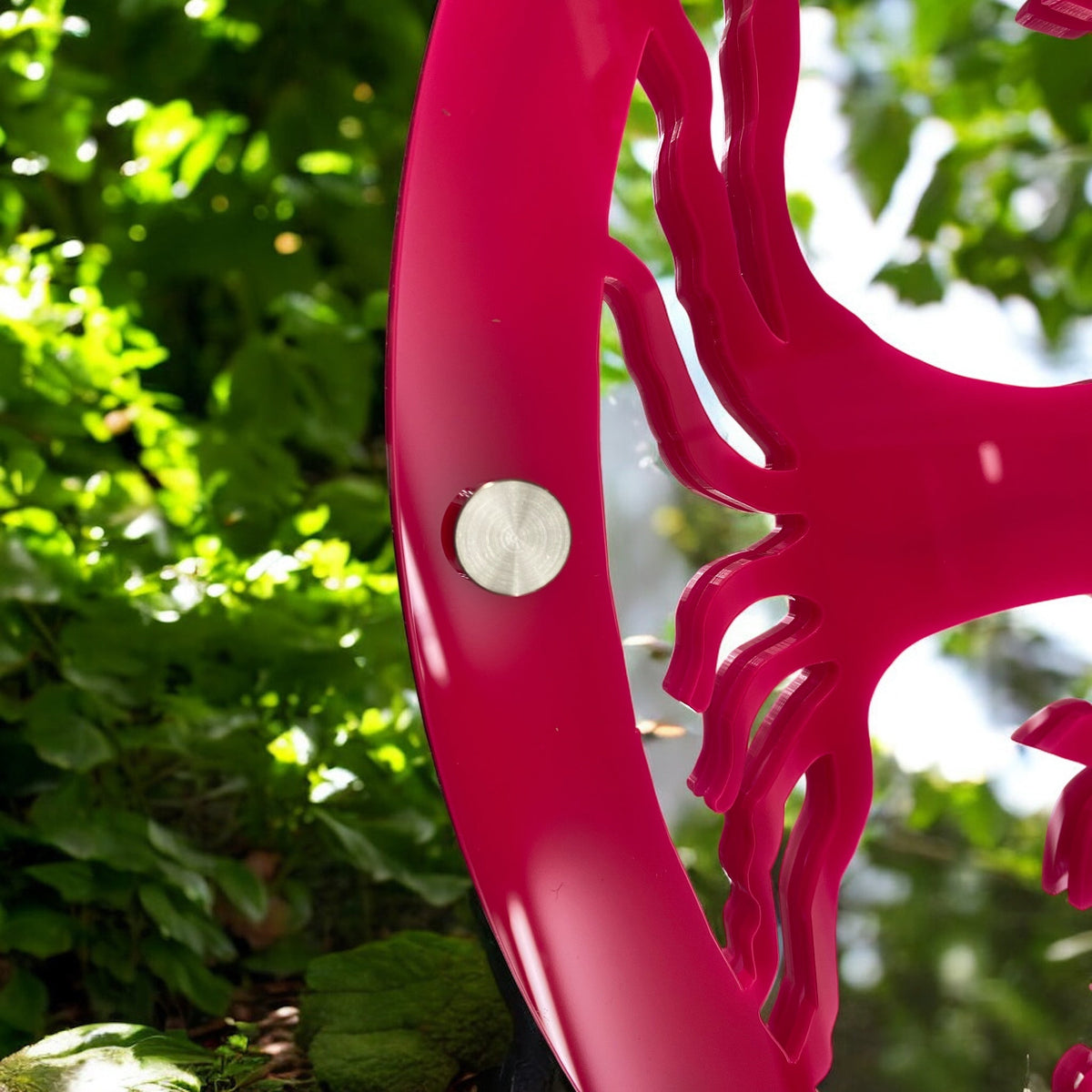 Close-up of a bright pink Tree of Life garden mirror with a silver mounting screw.