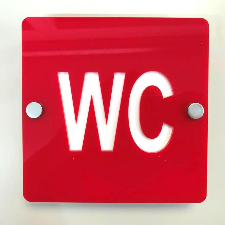 Square red toilet sign with white "WC" text and silver mounting standoffs.