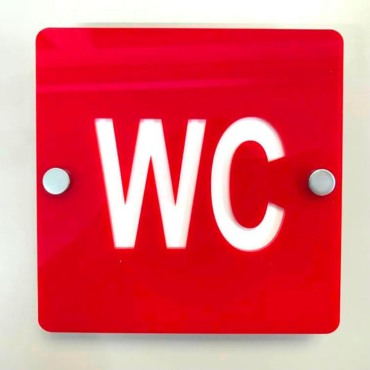 Square red toilet sign with white "WC" text and silver mounting standoffs.