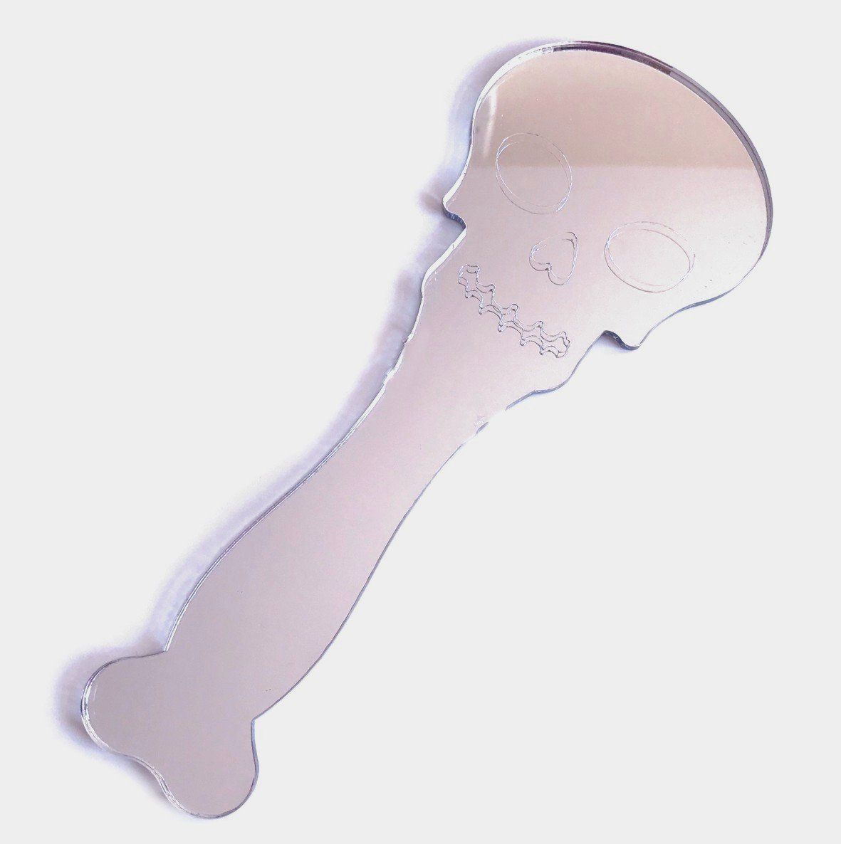 Silver skull-shaped hand-held mirror with engraved facial features and a bone-shaped handle on a white background.