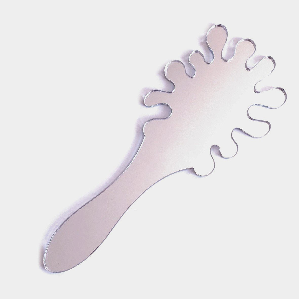 A splash-shaped silver hand-held mirror with a wavy, irregular edge and integrated handle on a white background.