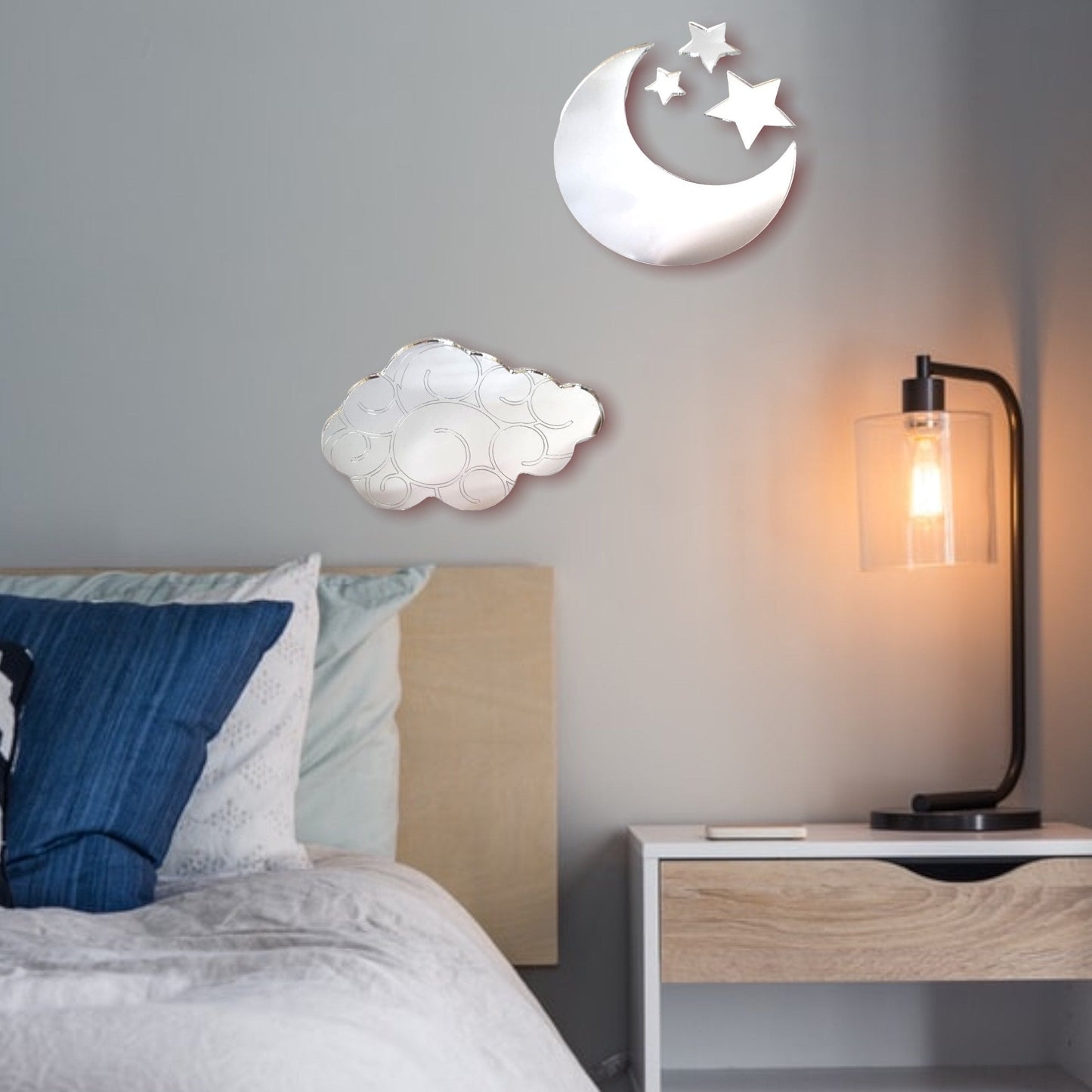 Crescent moon, star, and cloud shaped mirrors mounted on a bedroom wall above a bed and nightstand.