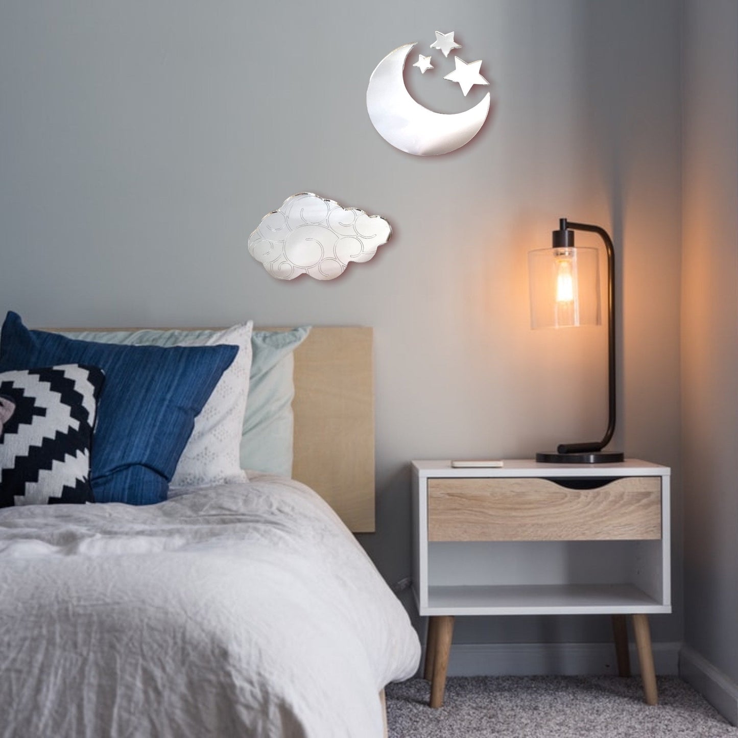 Cloud, moon, and star shaped wall mirrors mounted above a bed and nightstand.