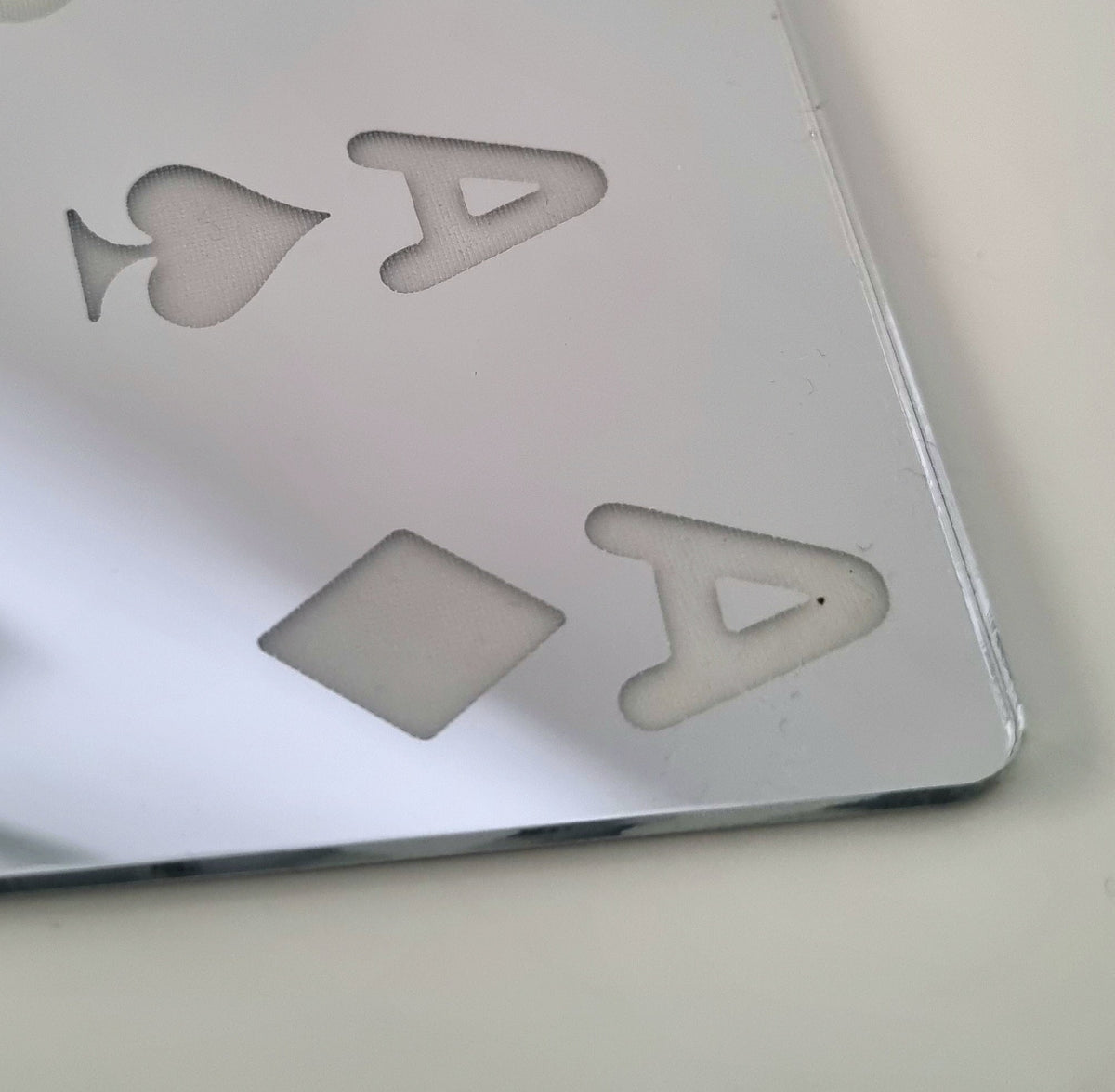 Close-up of the Aces High Mirror, featuring etched playing card suits and letters on reflective silver acrylic.