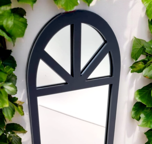 Dark gray Victorian arch framed garden mirror mounted on a white wall, flanked by green ivy.