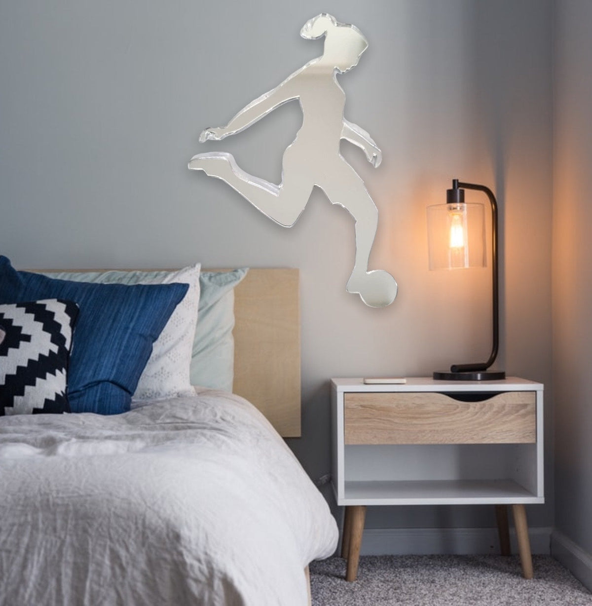 Female footballer-shaped wall mirror mounted above a bed in a bedroom.