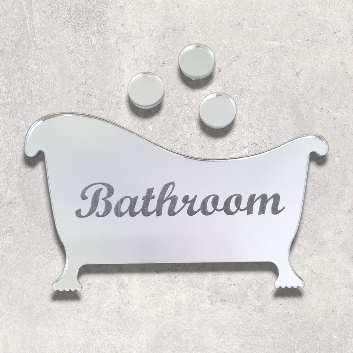 Mirrored bathtub-shaped sign with engraved "Bathroom" text and three mirrored bubbles above on gray surface.