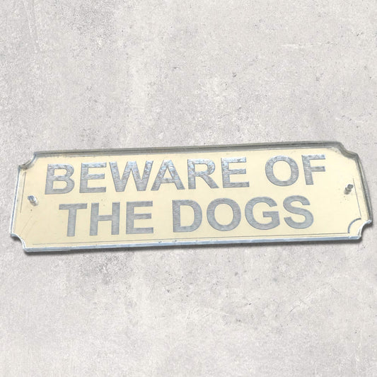 Rectangular mirror sign with silver text reading "BEWARE OF THE DOGS" on a neutral background.