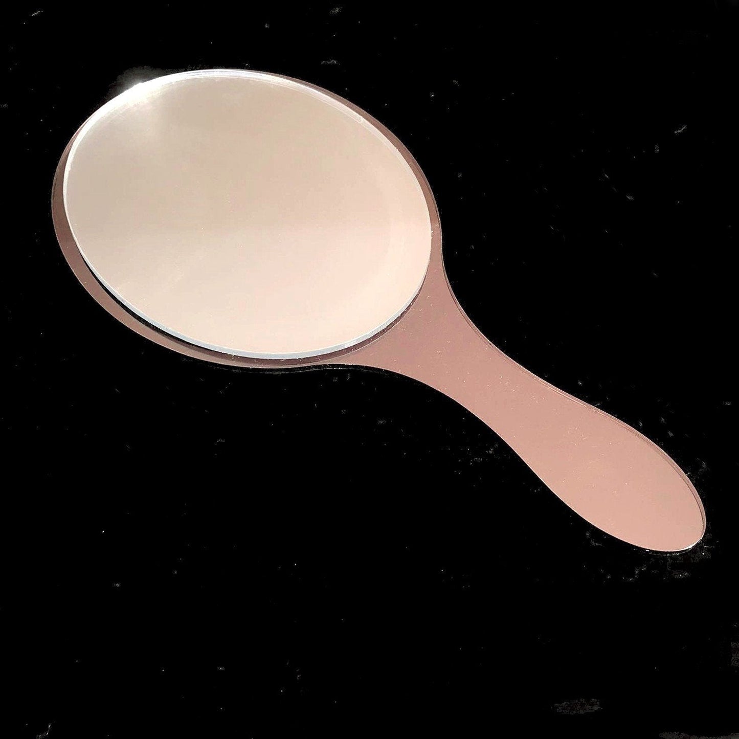 Oval hand-held mirror with a pinkish-brown handle and frame on a black background.