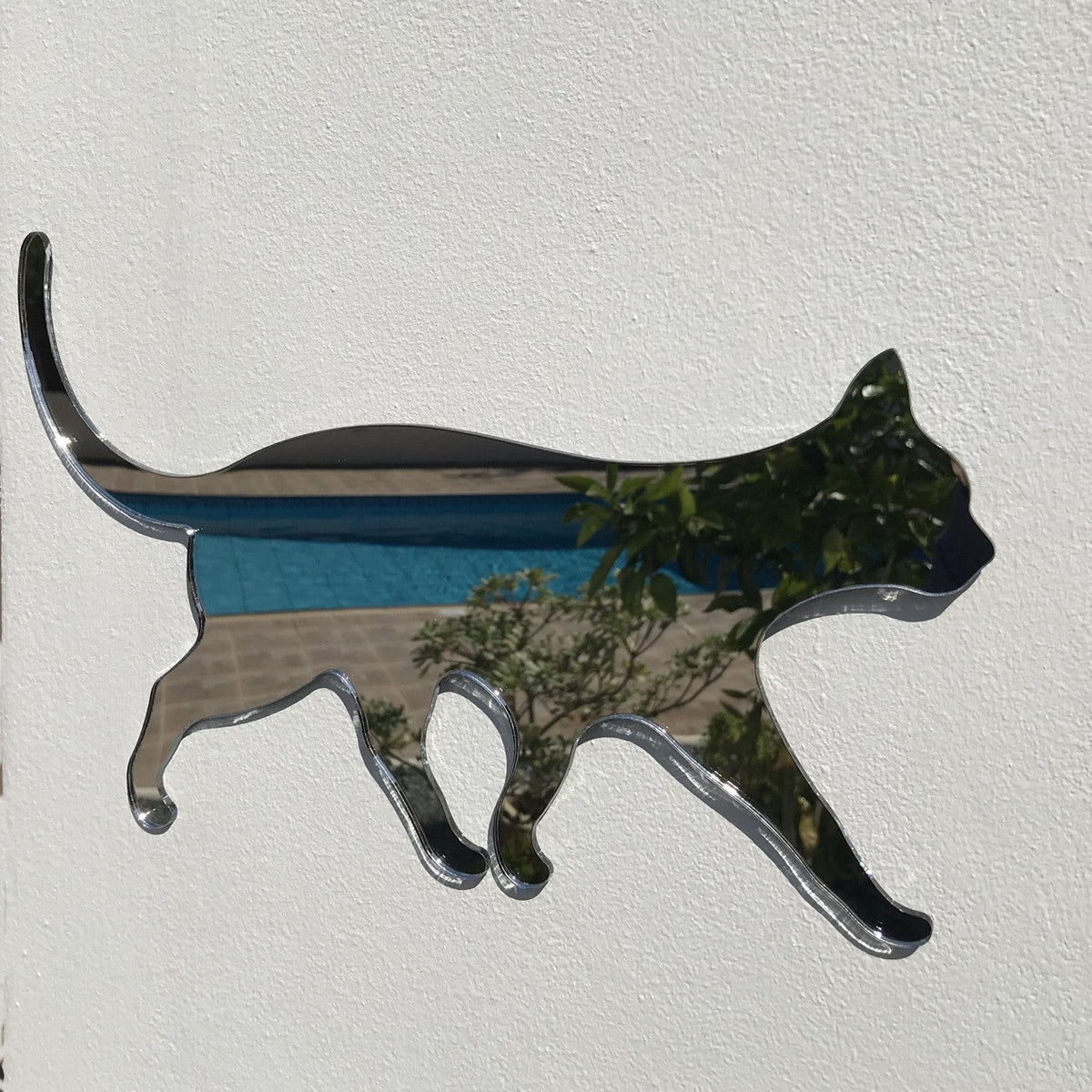 Cat-shaped acrylic garden mirror mounted on a white textured wall.