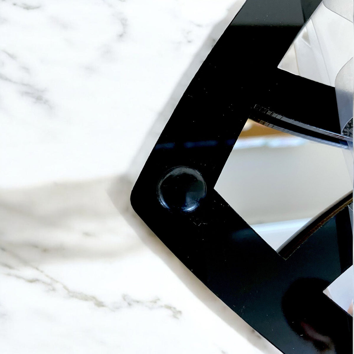 Close-up of a black Welcome Sign Framed Garden Mirror on a white marble surface.