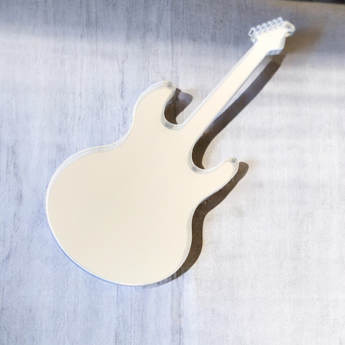 An electric guitar-shaped mirror on a textured grey background.