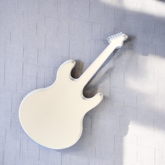 A reflective electric guitar-shaped wall mirror resting on a textured gray surface.