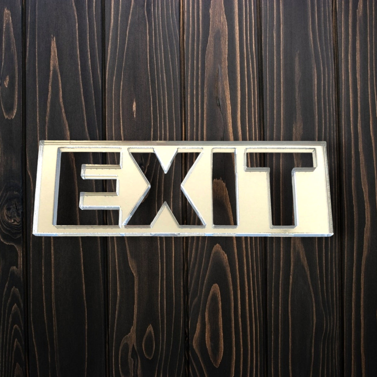 Rectangular mirrored acrylic exit sign mounted on a dark wood plank wall.